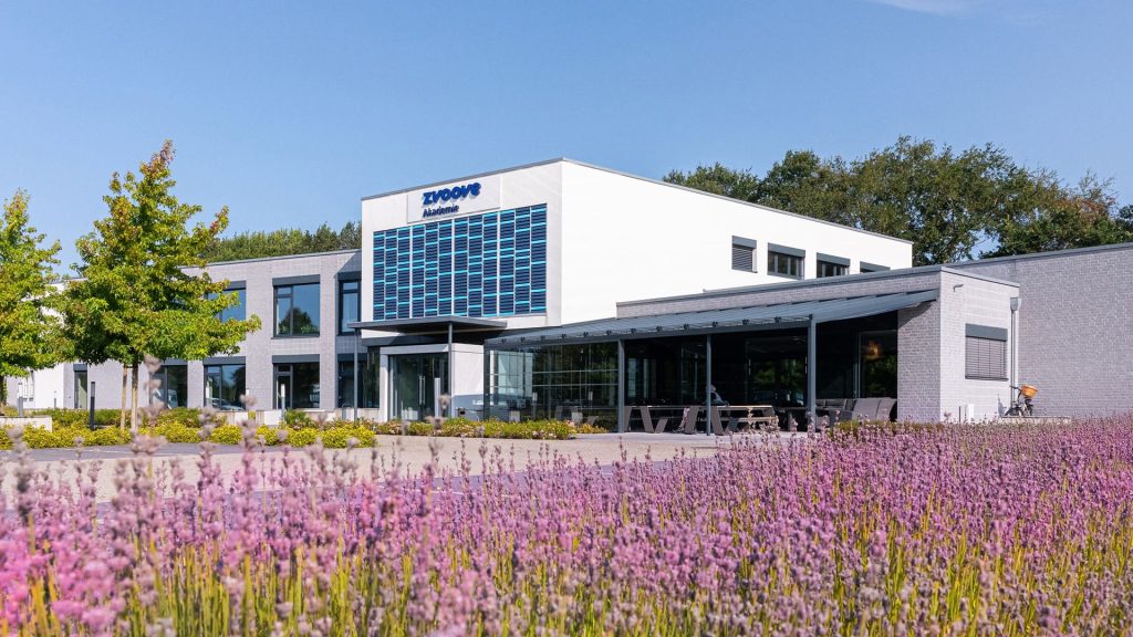 weißes Hauptgebäude von zvoove vor einer blühenden Wiese